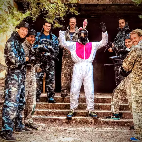 Group of paintball players surrounding their friend dressed in retro clothes.