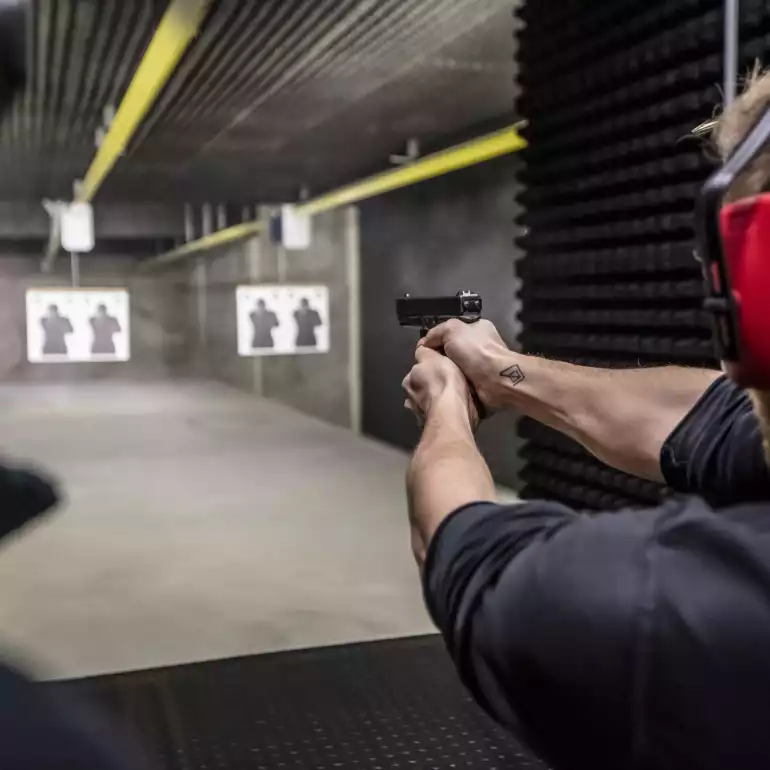 Person shooting from a pistol at a gun under under the supervision of an instructor.