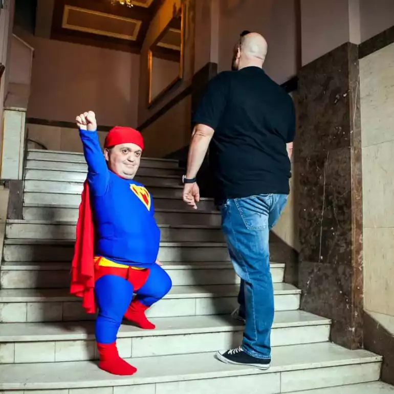 Dwarf entertaining dressed up in superman costume walking up the stairs.